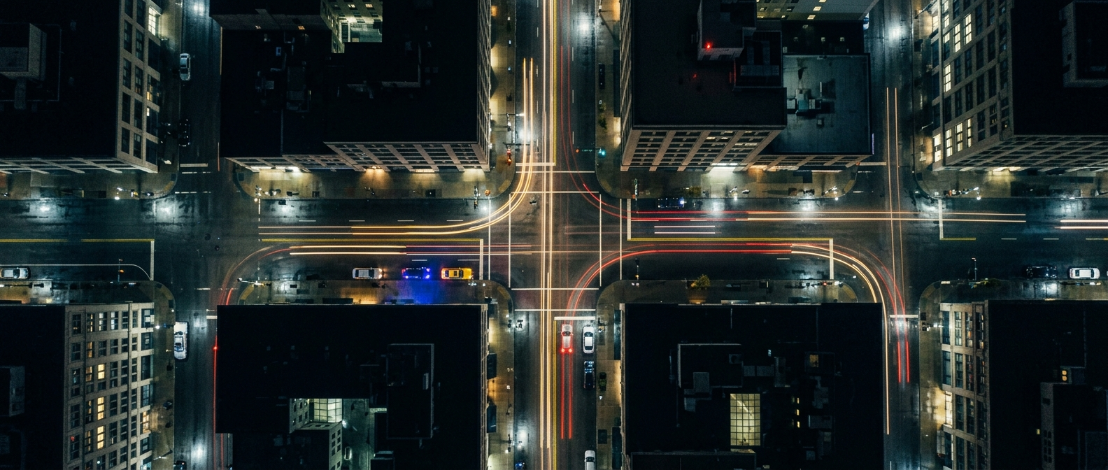 A rain-wet city intersection seen from high above at night, with long light trails from traffic